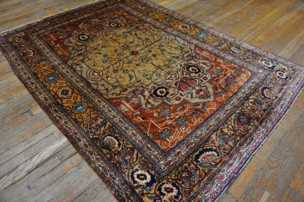 Traditional rug in gold, rust, and navy floral patterns rests on weathered wood plank flooring.