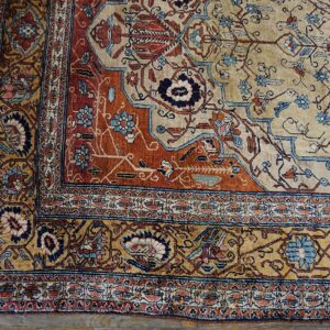 Detailed view of a low-pile rug featuring beige, rust, and blue floral patterns on gray wood flooring.