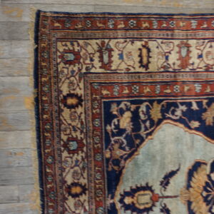 Traditional rug corner in navy, terracotta, and tan rests on distressed gray plank wood flooring.