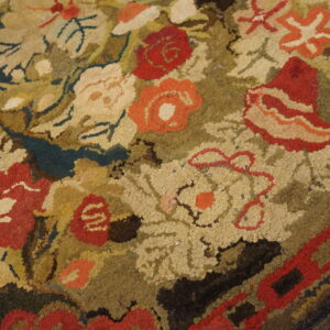 Highly textured hooked rug showing a dense floral pattern of red, orange, cream, and olive colors.