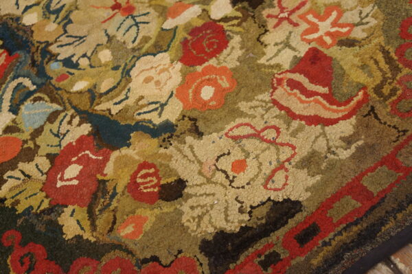 Highly textured hooked rug showing a dense floral pattern of red, orange, cream, and olive colors.