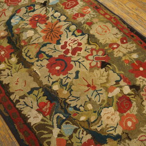 Muted floral rug featuring large red and orange blooms, green leaves, and a red border on wood planks.