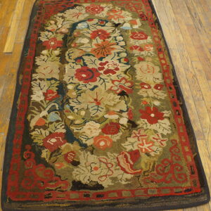 High-pile hooked rug displaying red and cream florals on an olive green field over light wood planks.