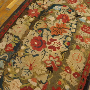 Textured rug with dense floral pattern in red, gold, olive, and blue on distressed wooden flooring.