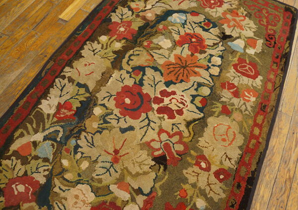 Textured rug with dense floral pattern in red, gold, olive, and blue on distressed wooden flooring.