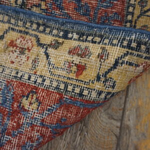 Detail of a low-pile rug with red, blue, and yellow geometric patterns on weathered wood planks.