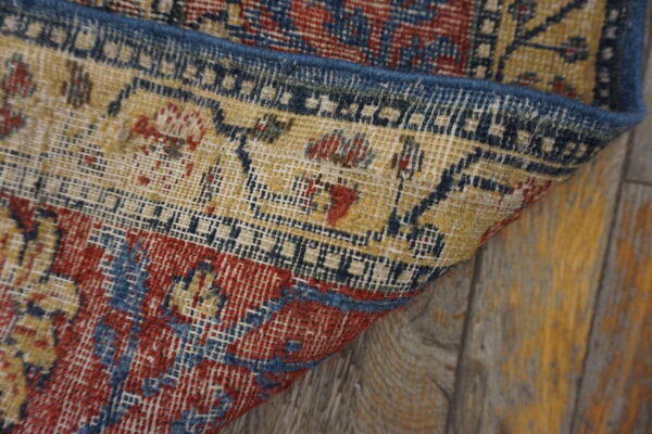 Detail of a low-pile rug with red, blue, and yellow geometric patterns on weathered wood planks.