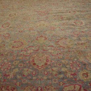 Large traditional rug with muted red, beige, and slate blue floral patterns laid flat on a wood floor.