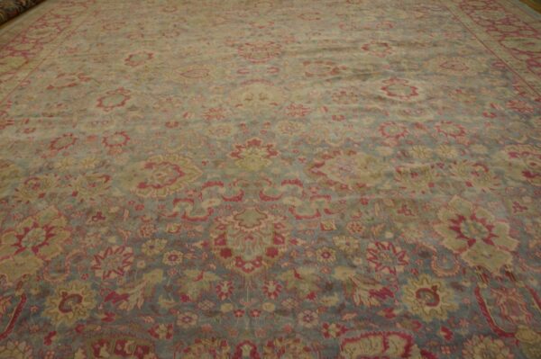 Large traditional rug with muted red, beige, and slate blue floral patterns laid flat on a wood floor.