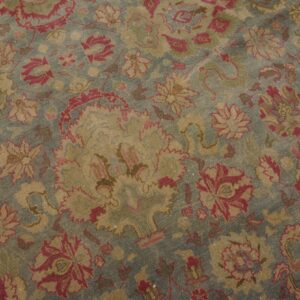 Low-pile rug with faded blue background and distressed rose and gold traditional floral patterns.