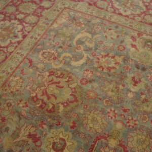 Distressed low-pile rug featuring a traditional floral pattern in dusty blue, deep red, and golden tan.