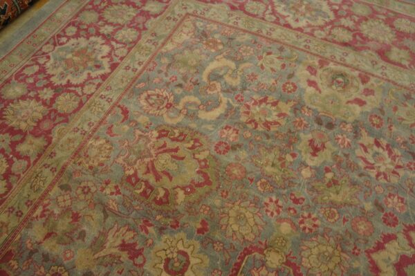 Distressed low-pile rug featuring a traditional floral pattern in dusty blue, deep red, and golden tan.