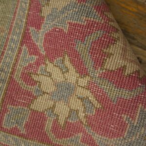 Flatwoven rug with geometric pink, beige, gray, and green patterns, curled up on a wood floor.