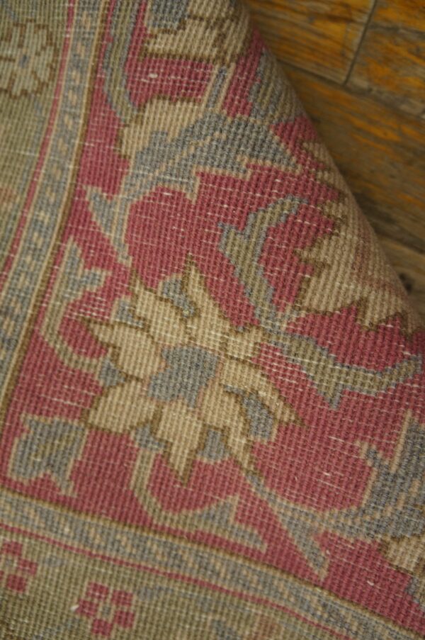 Flatwoven rug with geometric pink, beige, gray, and green patterns, curled up on a wood floor.