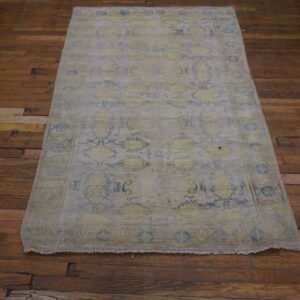 Faded traditional rug in pale gray, yellow, and blue rests on rustic dark wood flooring.