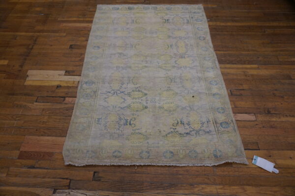 Faded traditional rug in pale gray, yellow, and blue rests on rustic dark wood flooring.