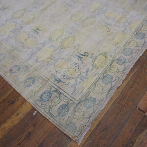 Pale low-pile rug with faded blue and yellow traditional patterns rests on rustic wood planks.