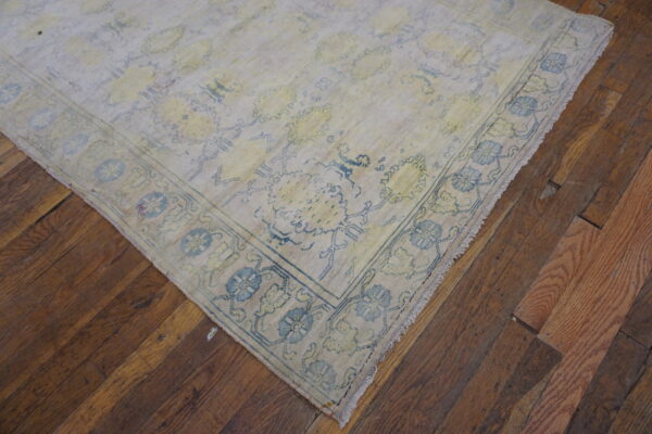 Pale low-pile rug with faded blue and yellow traditional patterns rests on rustic wood planks.