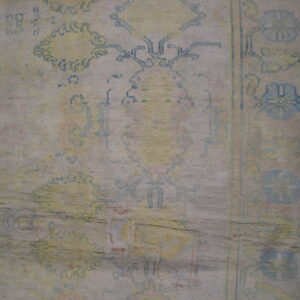 Distressed, low-pile rug close-up showing blue and yellow faded patterns and horizontal creases on wood floor.