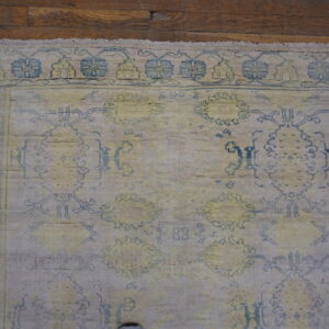 Low-pile rug in muted beige, blue, and yellow with traditional designs on dark wood floor.