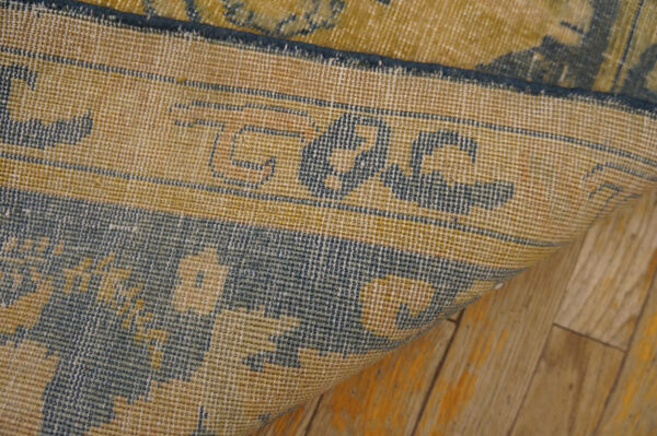 Tight weaving of a gold and dark blue patterned rug backing rests on distressed hardwood flooring.