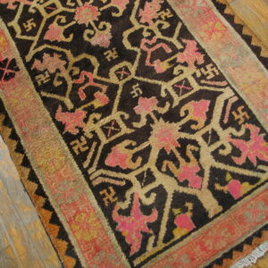 Dark rug with tan and bright pink geometric patterns and a broad red border on wood floor.