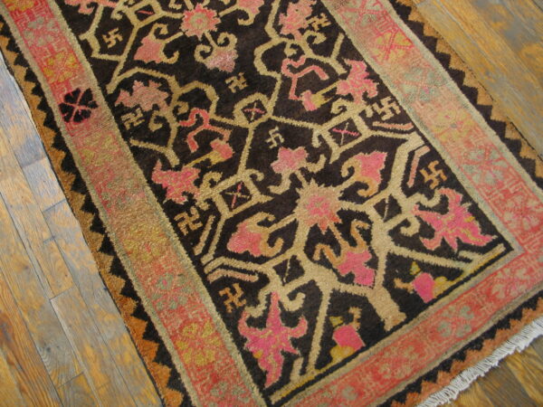 Dark rug with tan and bright pink geometric patterns and a broad red border on wood floor.