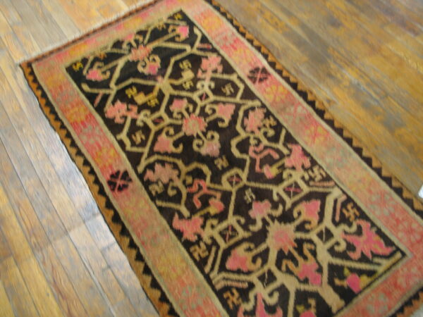 A dark brown runner rug with pink and gold geometric floral patterns rests on wide wooden floorboards.