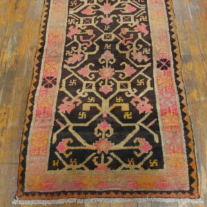 Geometric rug in dark brown, pink, and gold tones on a distressed wooden floor.
