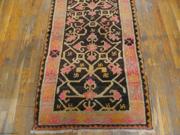 Geometric rug in dark brown, pink, and gold tones on a distressed wooden floor.