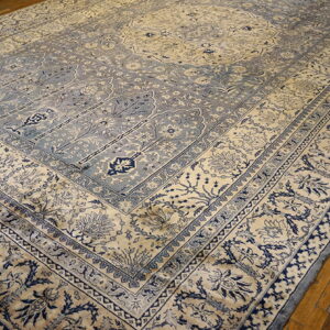 Ornate cream and dusty blue traditional rug featuring complex borders and a low pile is laid over wood flooring.