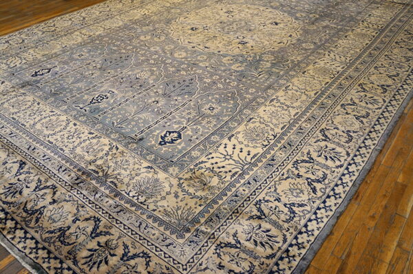 Ornate cream and dusty blue traditional rug featuring complex borders and a low pile is laid over wood flooring.