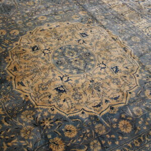 Muted blue and gold rug displaying a central circular medallion and complex floral border design.