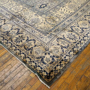 A tan and indigo floral patterned rug corner rests on rustic hardwood plank flooring.