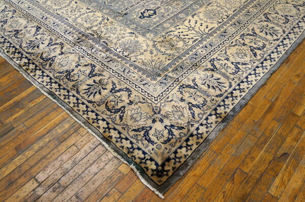 A tan and indigo floral patterned rug corner rests on rustic hardwood plank flooring.