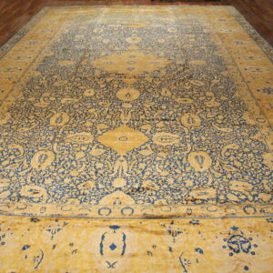 Ornate yellow and blue rug with floral patterns and a central medallion rests on wood flooring.