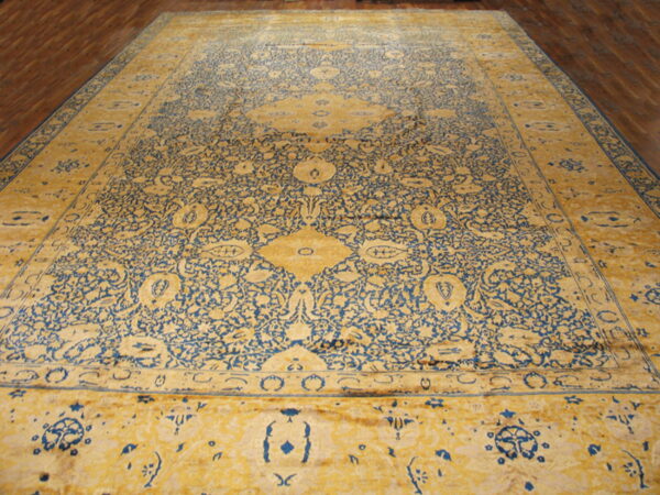 Ornate yellow and blue rug with floral patterns and a central medallion rests on wood flooring.