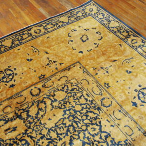 Detail of a traditional gold and navy rug border and field resting on polished wooden planks.