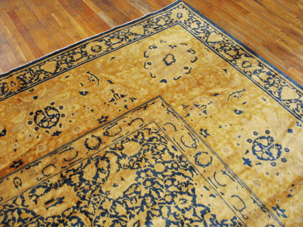 Detail of a traditional gold and navy rug border and field resting on polished wooden planks.