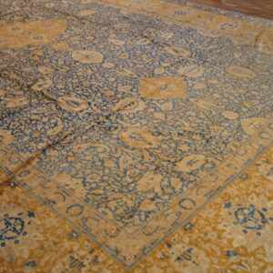 Traditional rug with dense blue and ochre floral motifs and a detailed border on a wood floor.