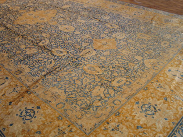Traditional rug with dense blue and ochre floral motifs and a detailed border on a wood floor.