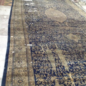 Long navy rug featuring tan floral and bird motifs, detailed border, on a concrete floor.