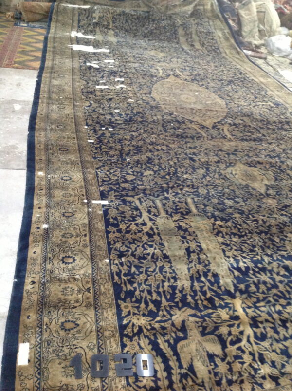 Long navy rug featuring tan floral and bird motifs, detailed border, on a concrete floor.