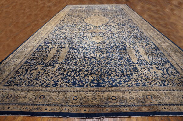Large navy blue and beige rug with a detailed botanical pattern lying on polished hardwood flooring.
