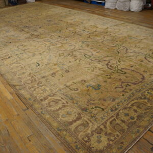 An oversized beige rug with muted green, blue, and brown floral patterns on wood floors.