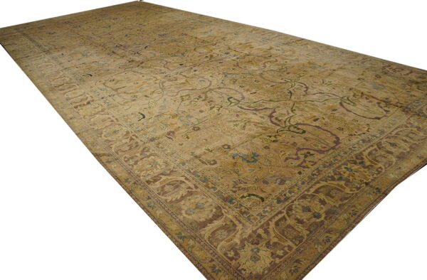 Muted gold and beige low-pile rug featuring a traditional ornate floral pattern and thick brown border.
