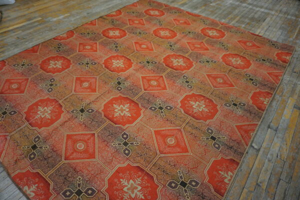 Intricate orange and brown tiled rug with floral and cross motifs displayed on rustic wood flooring.