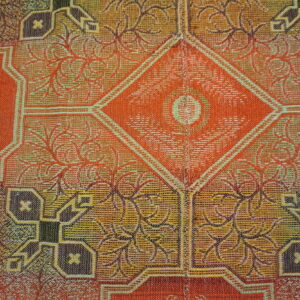 Detailed low-pile rug pattern featuring orange, gold, and brown geometric and branching floral designs.