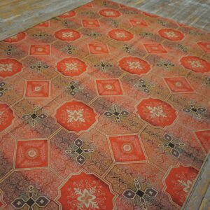 Orange and earth-toned rug with elaborate geometric patterns resting on rustic gray wood flooring.