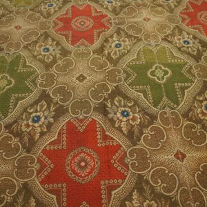 Ornate, low-pile rug detail showing alternating red and olive green medallions on a brown patterned field.